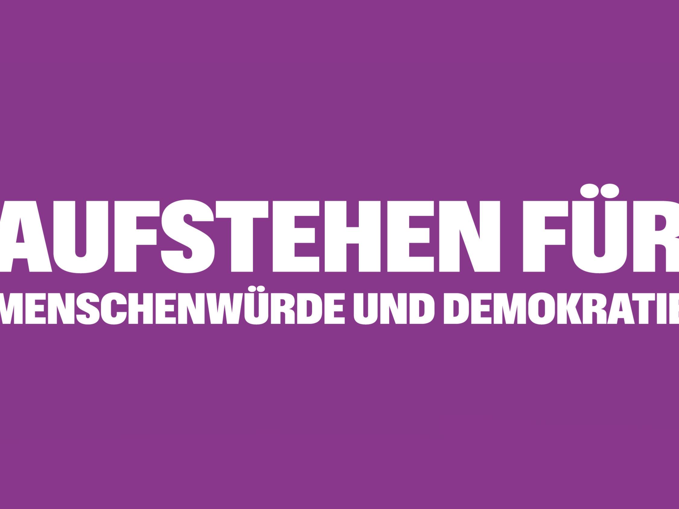 Auf lila Hintergrund steht Aufstehen für Menschenwürde und Demokratie; umrahmt von Ausrufezeichen