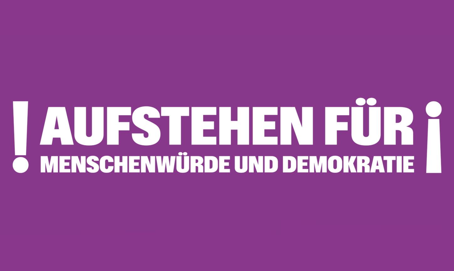 Auf lila Hintergrund steht Aufstehen für Menschenwürde und Demokratie; umrahmt von Ausrufezeichen