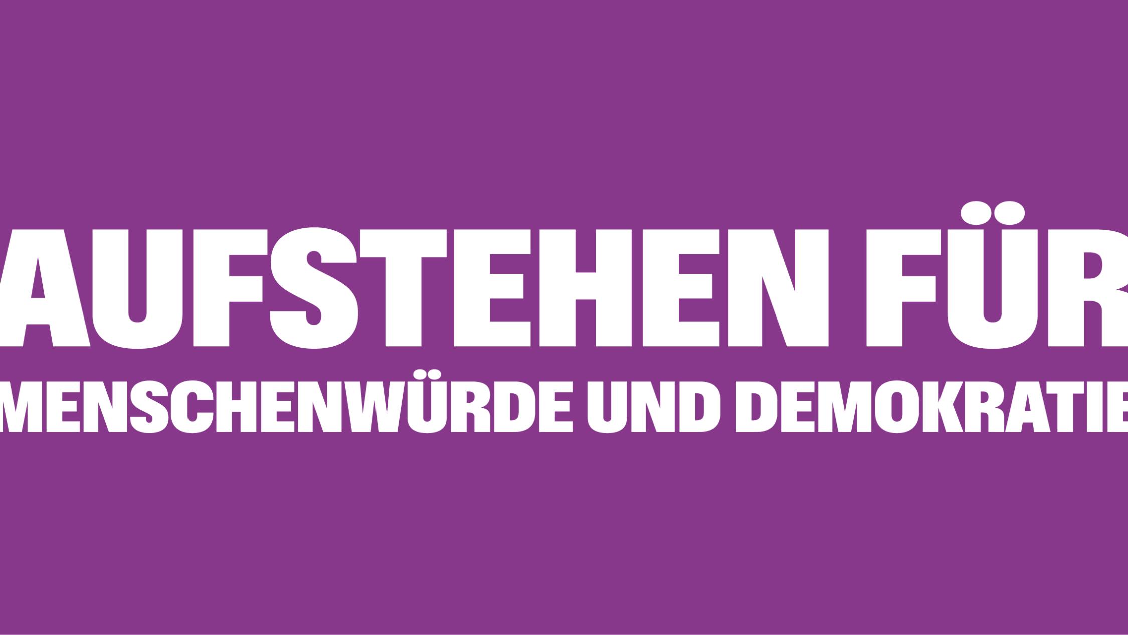 Auf einem lila Banner steht 'Aufstehen für Menschnwürde und Demokratie', rechts und links mit Ausrufezeichen umrahmt