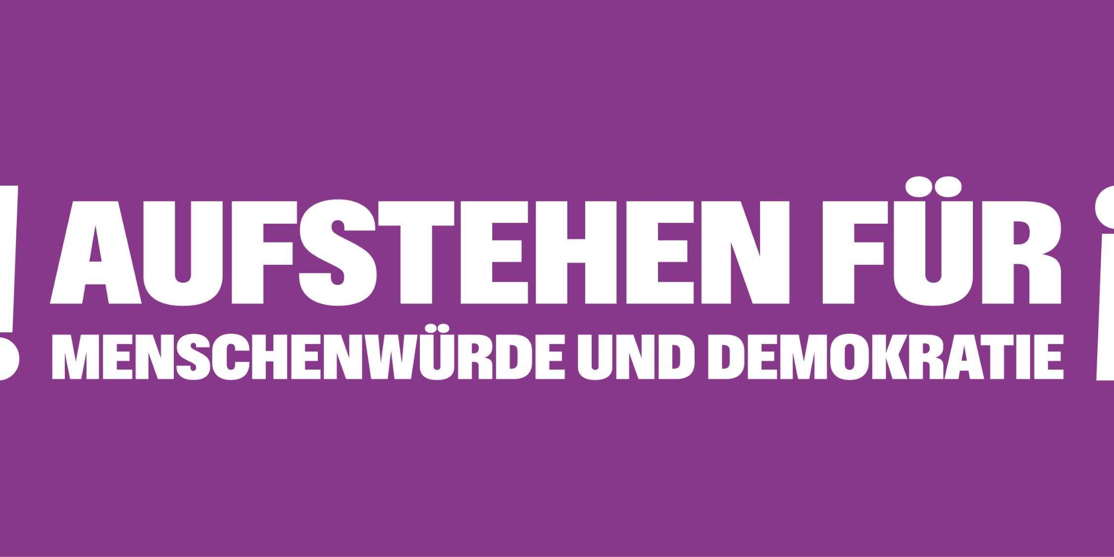 Auf einem lila Banner steht 'Aufstehen für Menschnwürde und Demokratie', rechts und links mit Ausrufezeichen umrahmt