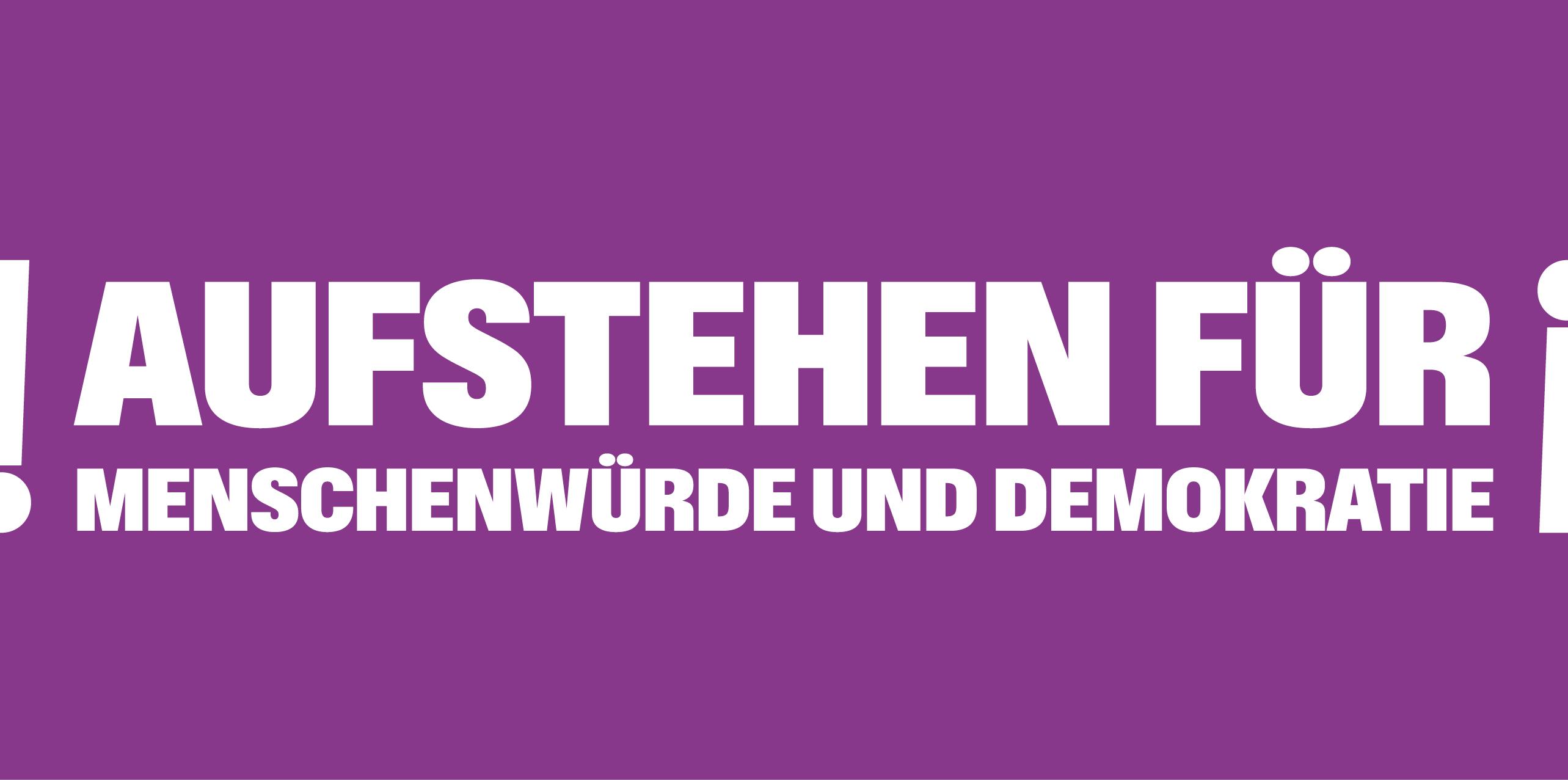 Auf einem lila Banner steht 'Aufstehen für Menschnwürde und Demokratie', rechts und links mit Ausrufezeichen umrahmt