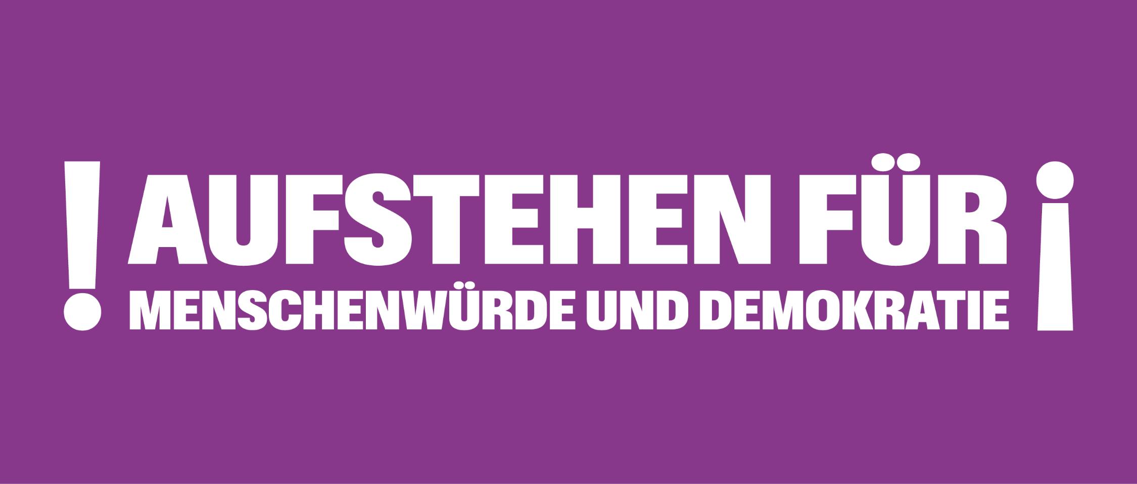 Auf einem lila Banner steht 'Aufstehen für Menschnwürde und Demokratie', rechts und links mit Ausrufezeichen umrahmt