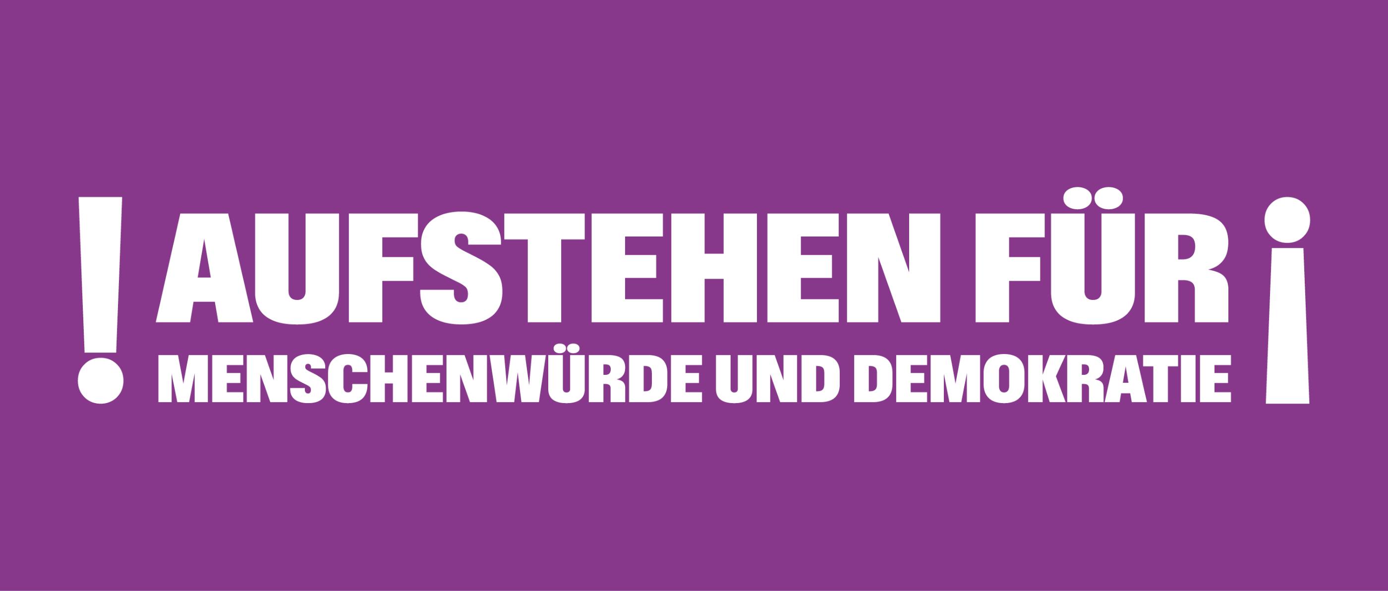 Auf einem lila Banner steht 'Aufstehen für Menschnwürde und Demokratie', rechts und links mit Ausrufezeichen umrahmt