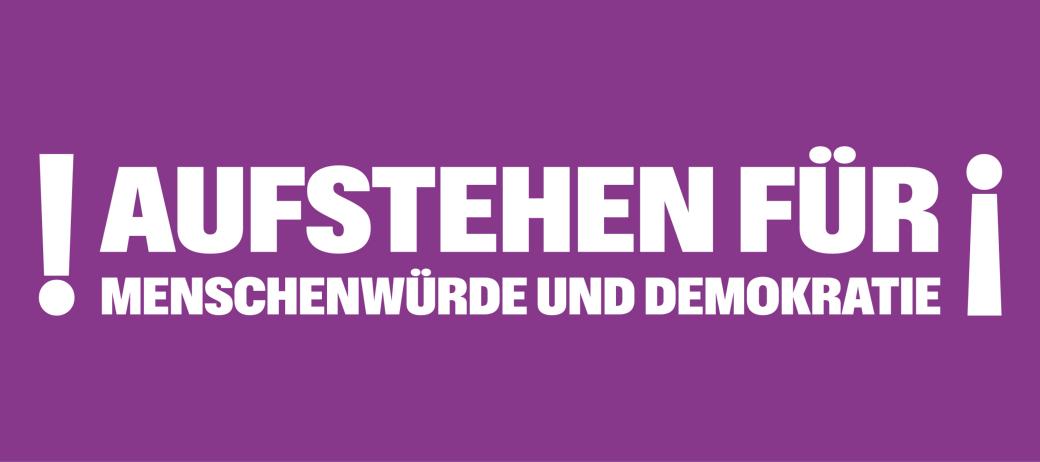 Auf einem lila Banner steht 'Aufstehen für Menschnwürde und Demokratie', rechts und links mit Ausrufezeichen umrahmt