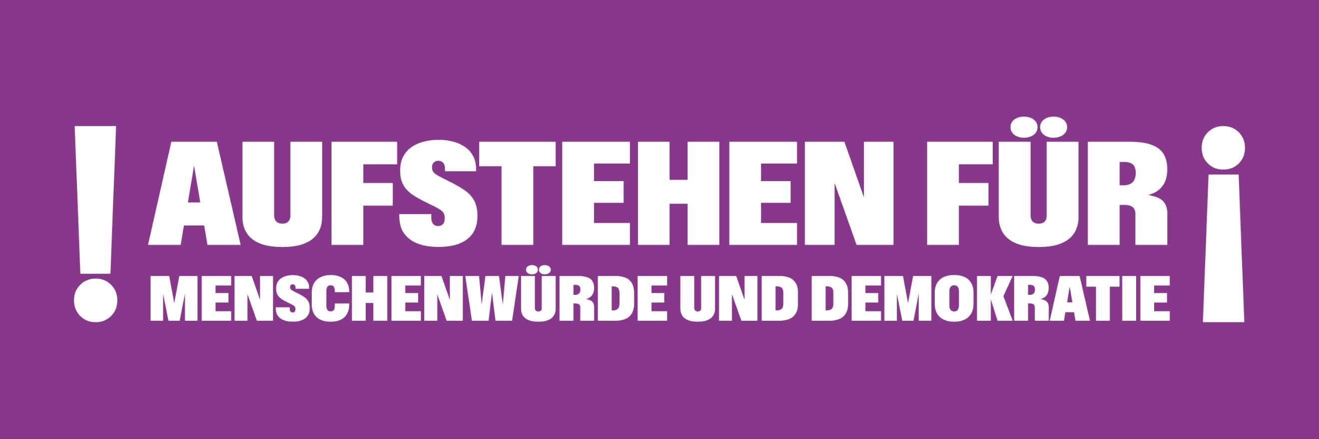 Auf einem lila Banner steht 'Aufstehen für Menschnwürde und Demokratie', rechts und links mit Ausrufezeichen umrahmt