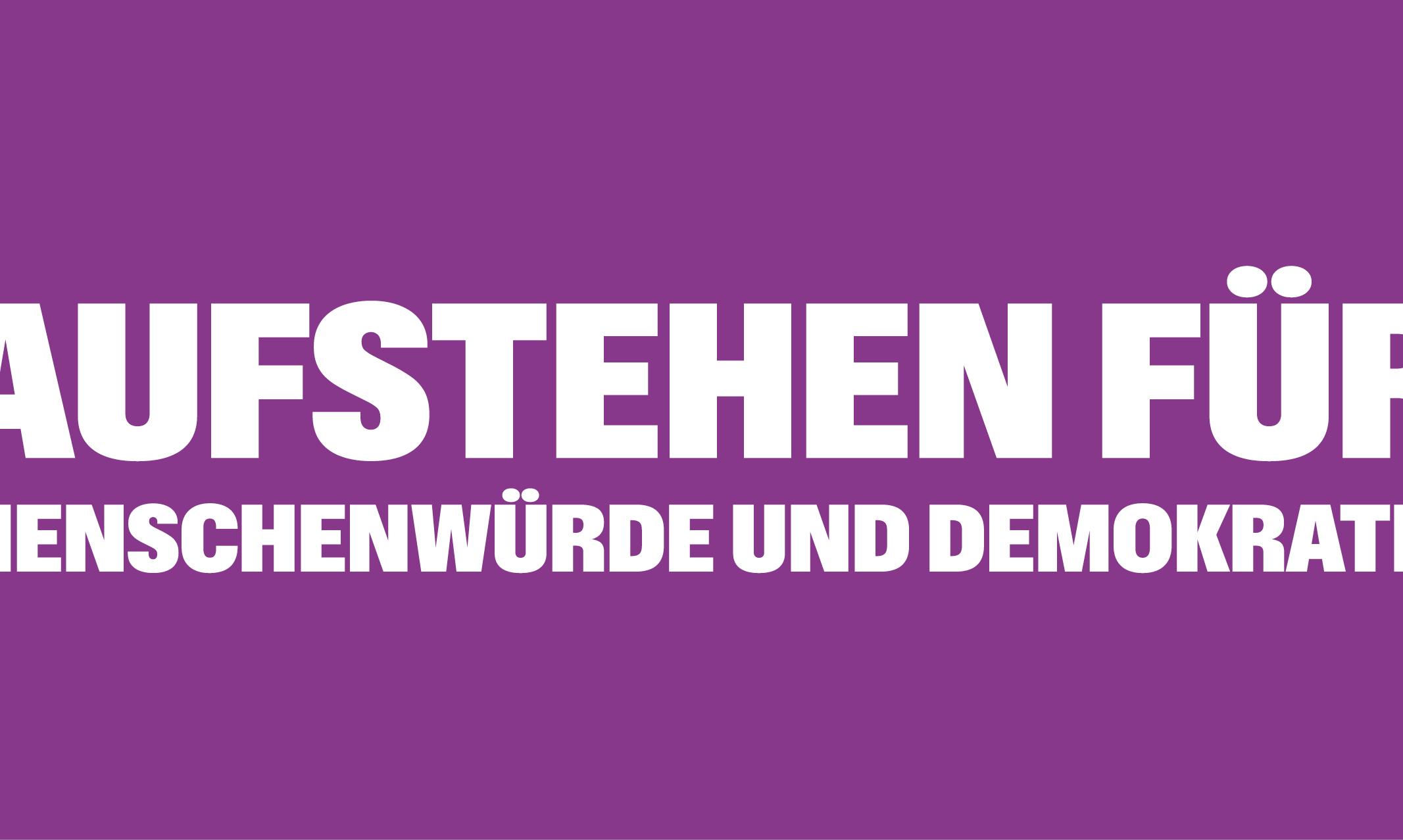Auf einem lila Banner steht 'Aufstehen für Menschnwürde und Demokratie', rechts und links mit Ausrufezeichen umrahmt
