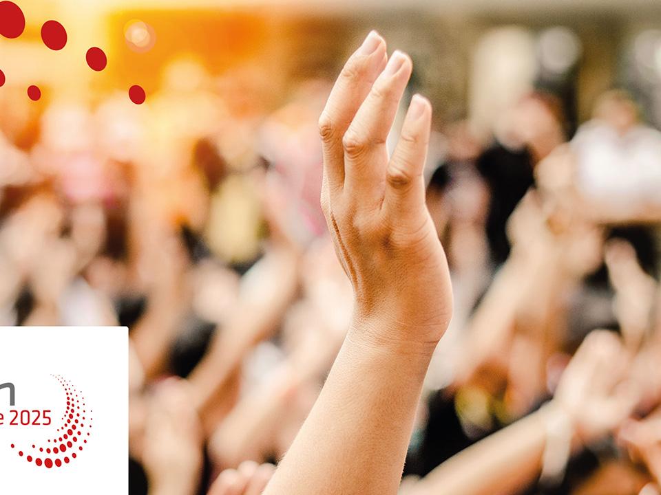 Eine Hand streckt sich in die Höhe, im Hintergrund sind verschwommen noch zahlreiche Menschen und hochgehobene Hände zu sehen.