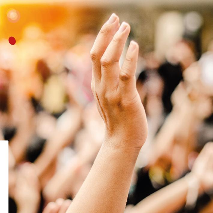 Eine Hand streckt sich in die Höhe, im Hintergrund sind verschwommen noch zahlreiche Menschen und hochgehobene Hände zu sehen.