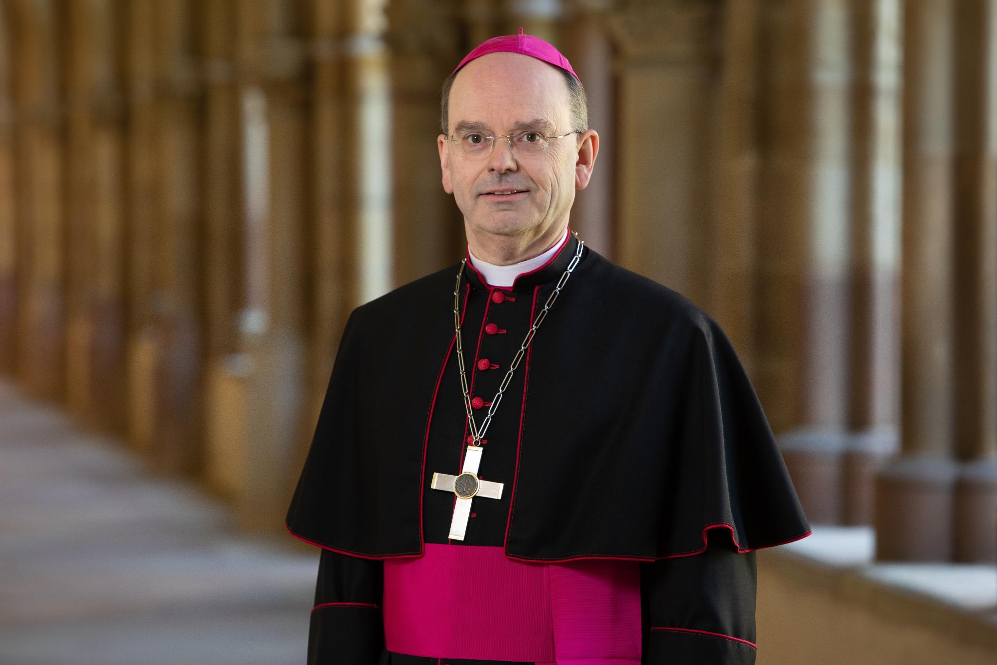 Hier ist Weihbischof Brahm lächelnd im Kreuzgang zusehen, zudem trägt er ein Ornat.