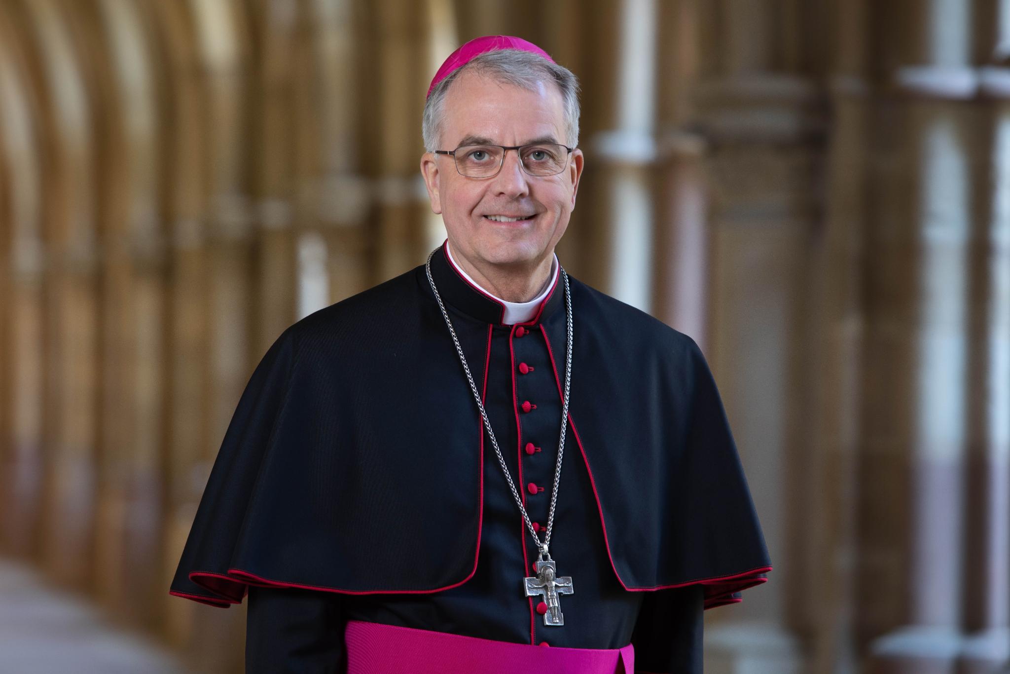 Hier ist Weihbischof Peters lächelnd im Kreuzgang zusehen, zudem trägt er ein Ornat.