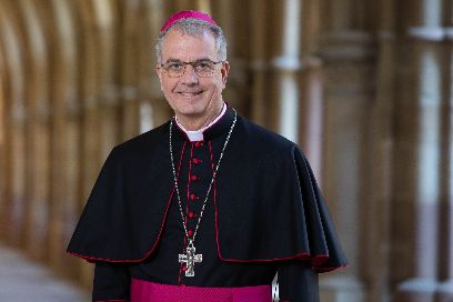 Hier ist Weihbischof Peters lächelnd im Kreuzgang zusehen, zudem trägt er ein Ornat.