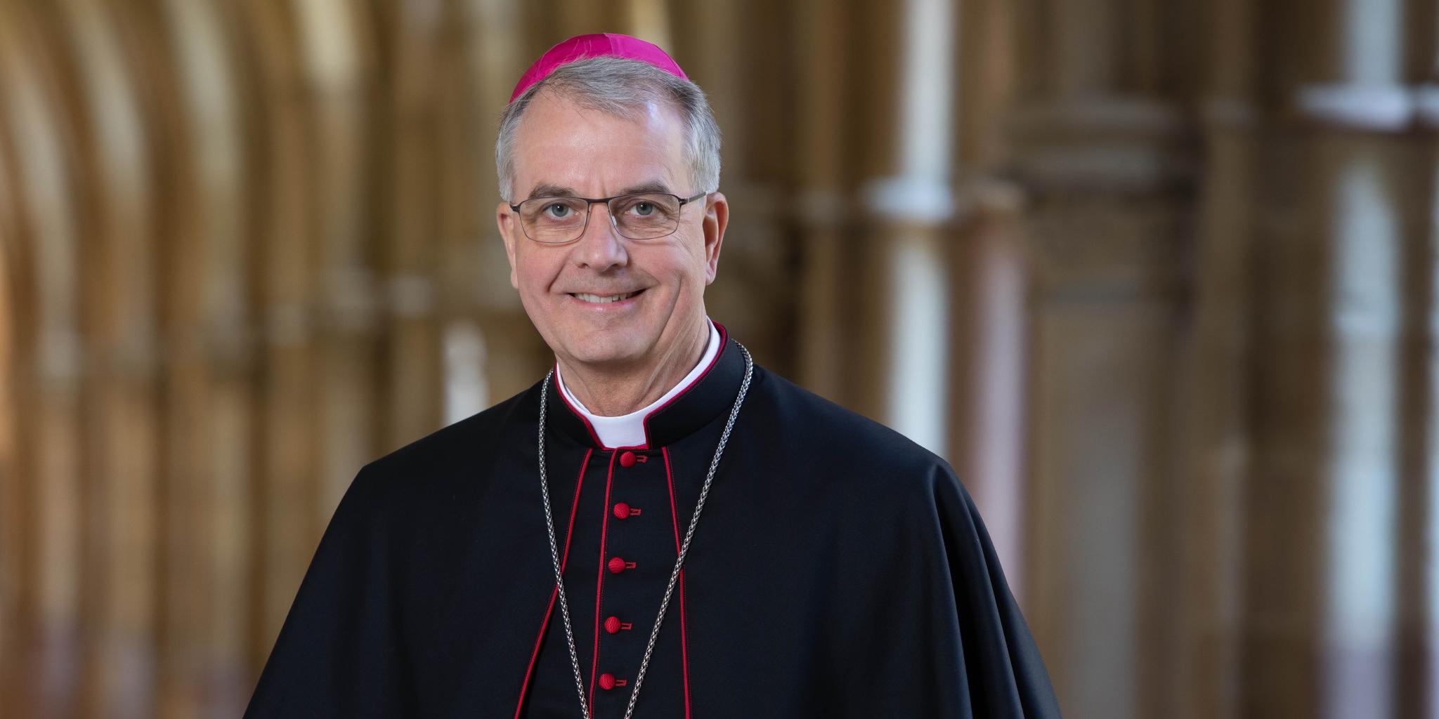 Hier ist Weihbischof Peters lächelnd im Kreuzgang zusehen, zudem trägt er ein Ornat.