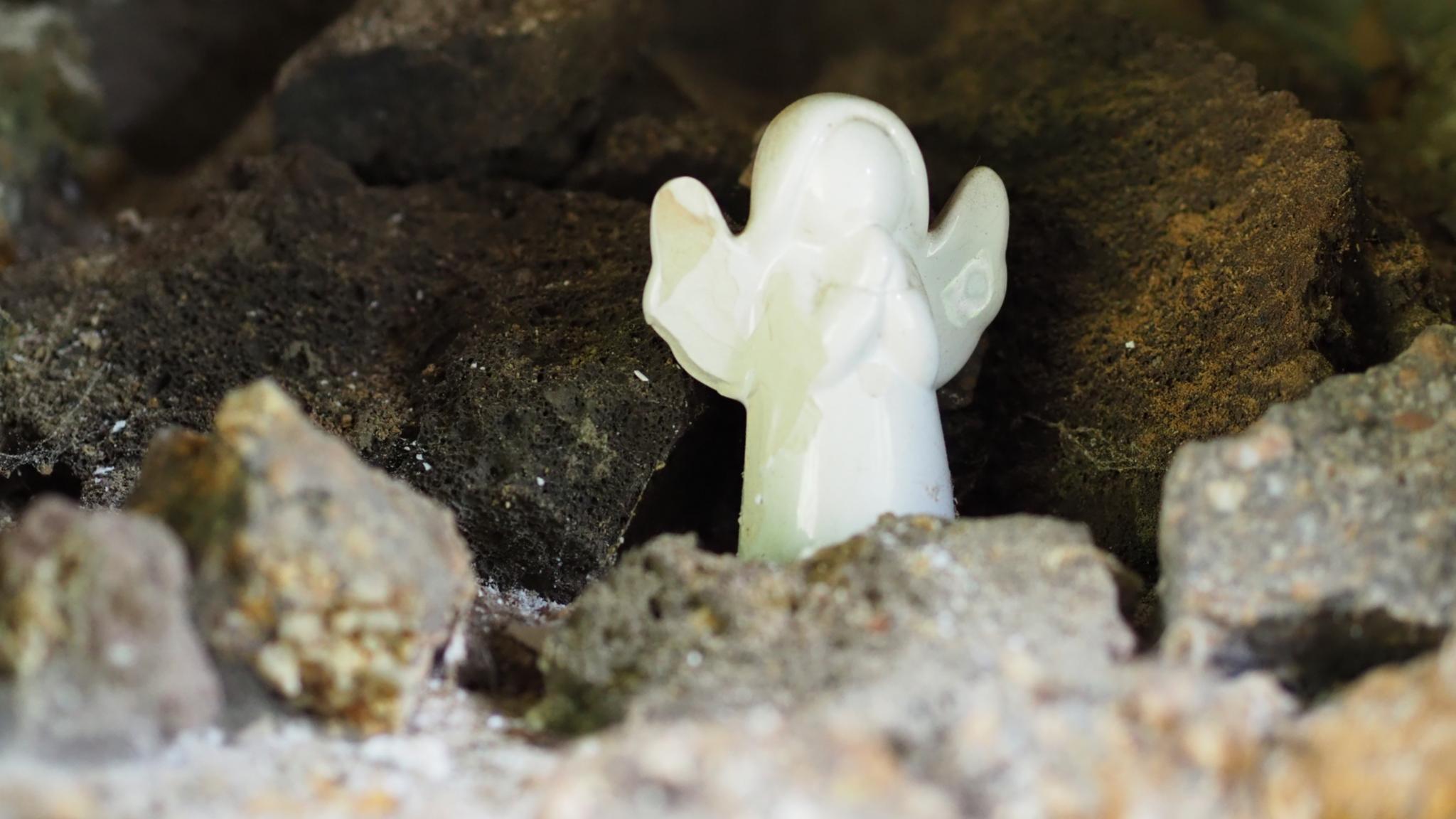 Ein kleiner weißer Engel steht zwischen Steinen