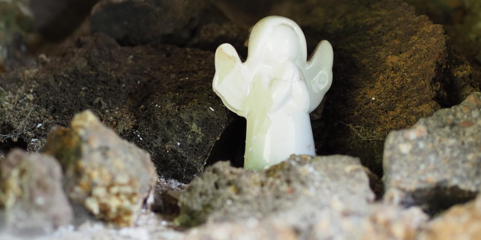 Ein kleiner weißer Engel steht zwischen Steinen