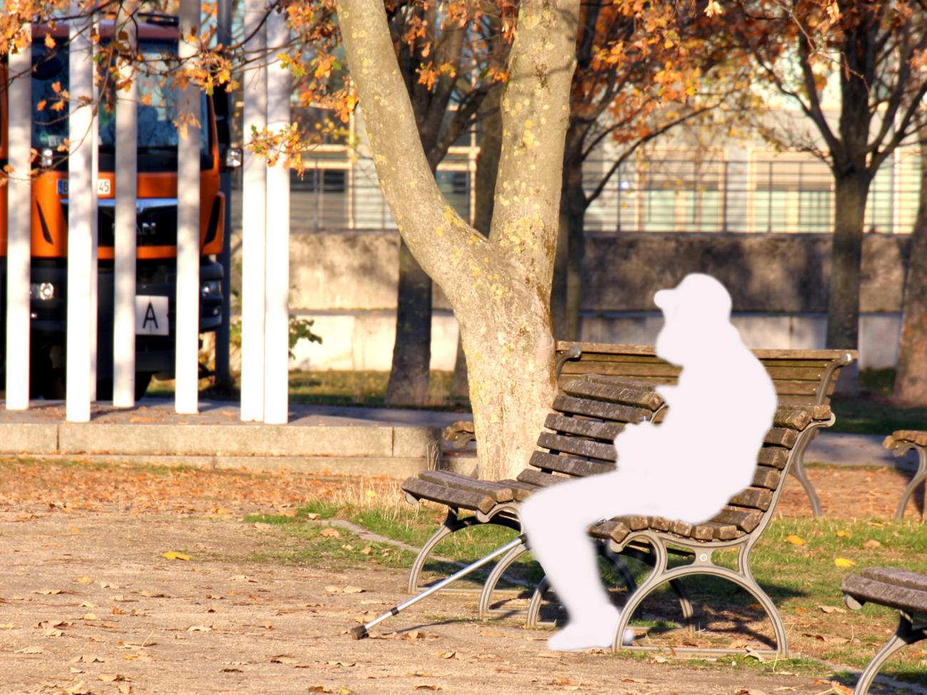 Auf einer Parkbank sitzt eine Person in Form einer weißen Figur, die einen Menschen schemenhaft darstellt.