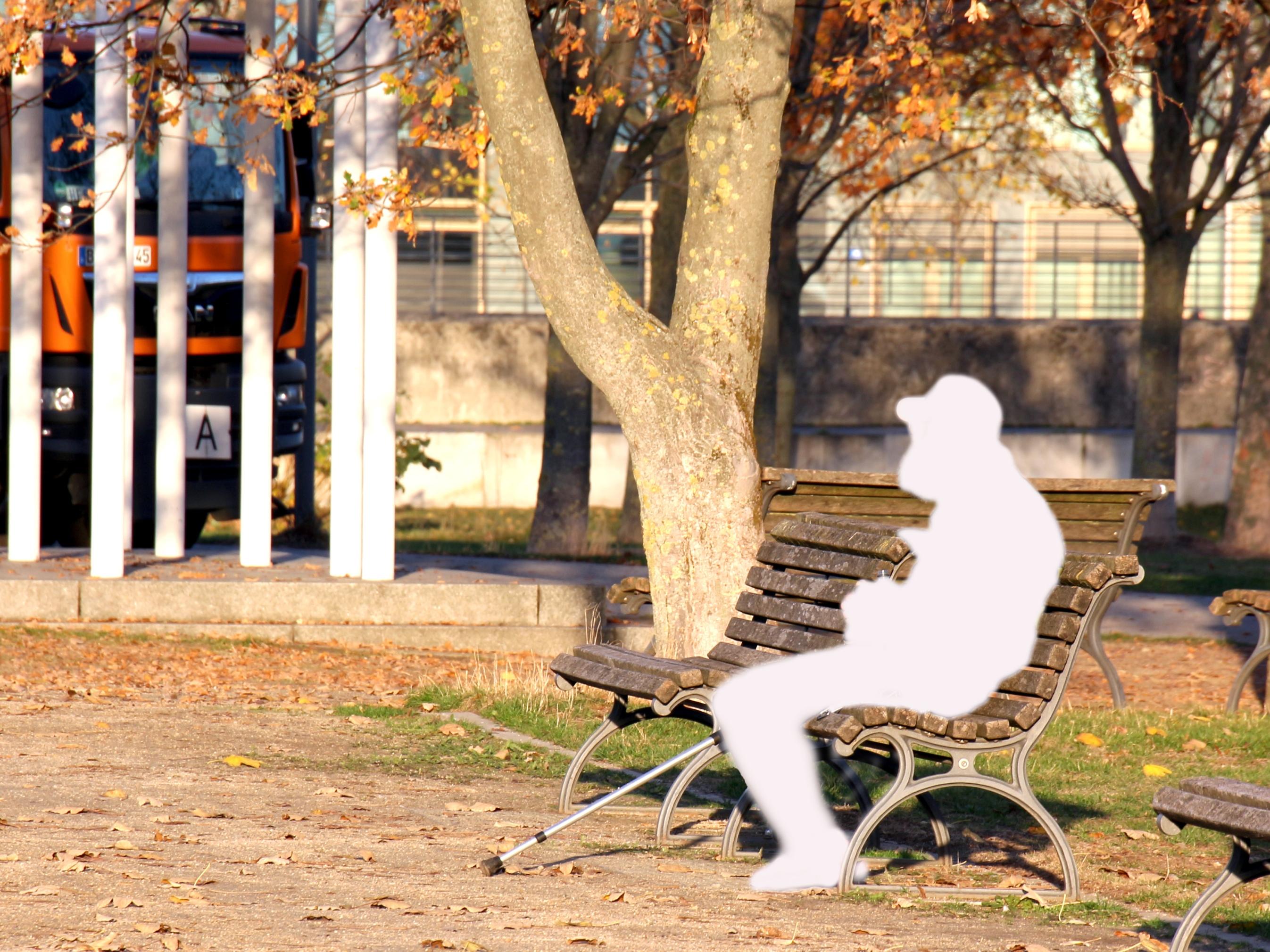 Auf einer Parkbank sitzt eine Person in Form einer weißen Figur, die einen Menschen schemenhaft darstellt.