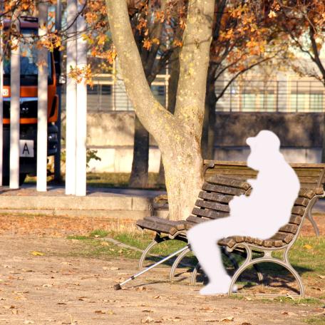 Auf einer Parkbank sitzt eine Person in Form einer weißen Figur, die einen Menschen schemenhaft darstellt.