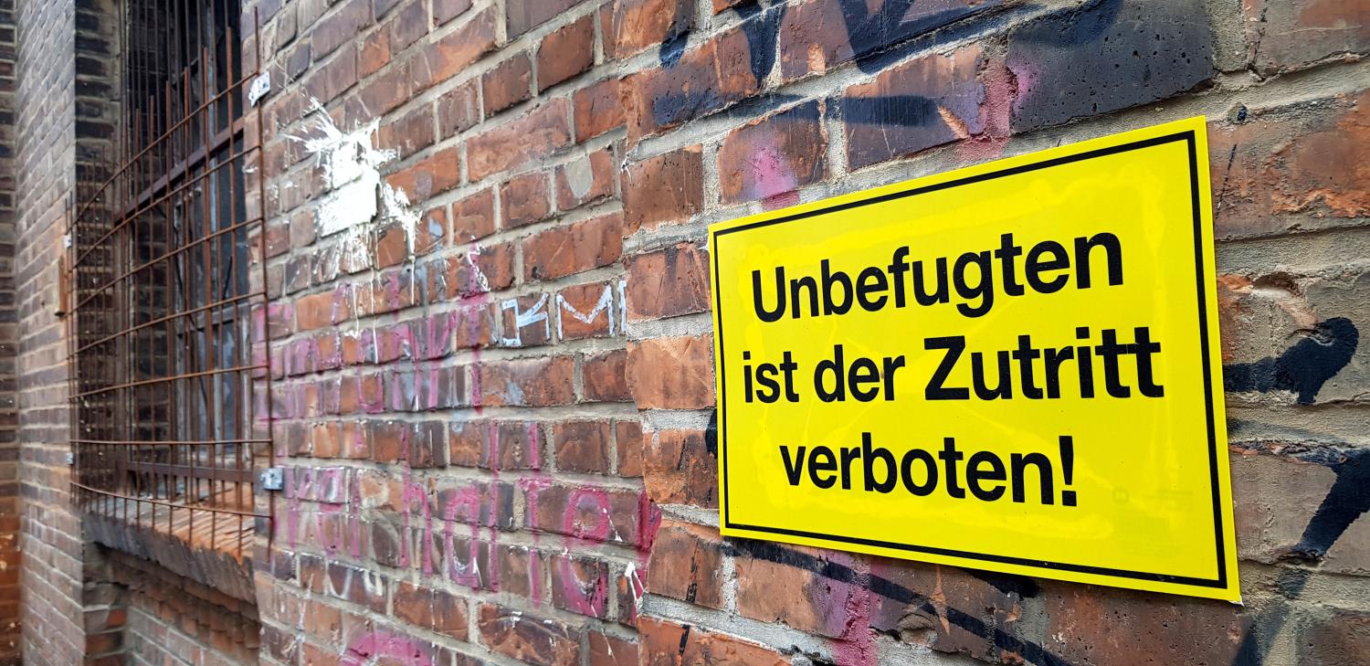 Man sieht eine Mauer mit einem Warnschild: Unbefugten ist der Zutritt verboten.