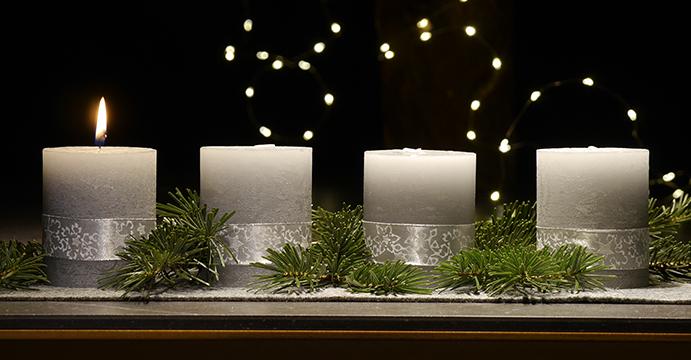 An einem Adventsgesteck brennt eine Kerze