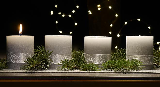 An einem Adventsgesteck brennt eine Kerze
