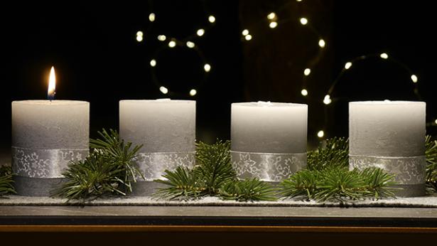 An einem Adventsgesteck brennt eine Kerze