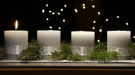 An einem Adventsgesteck brennt eine Kerze
