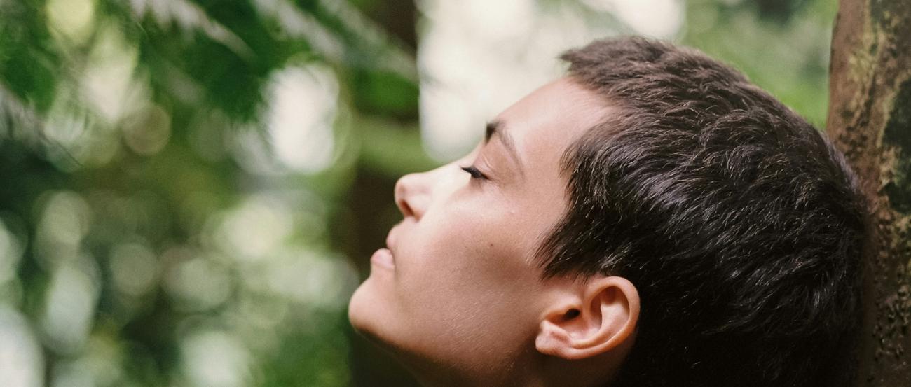 Atem holen (c) Motoki Tonn auf unsplash.com Eine Frau steht im Wald an einen Baum gelehnt und atmet tief ein