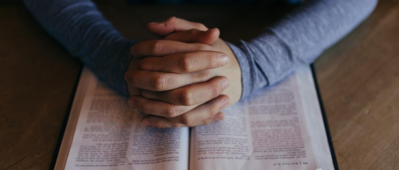 Symbolbild (c) Patrick Fore / unsplash Man sieht eine aufgeschlagene Bibel. Darauf liegen zum Gebet gefaltete Hände.