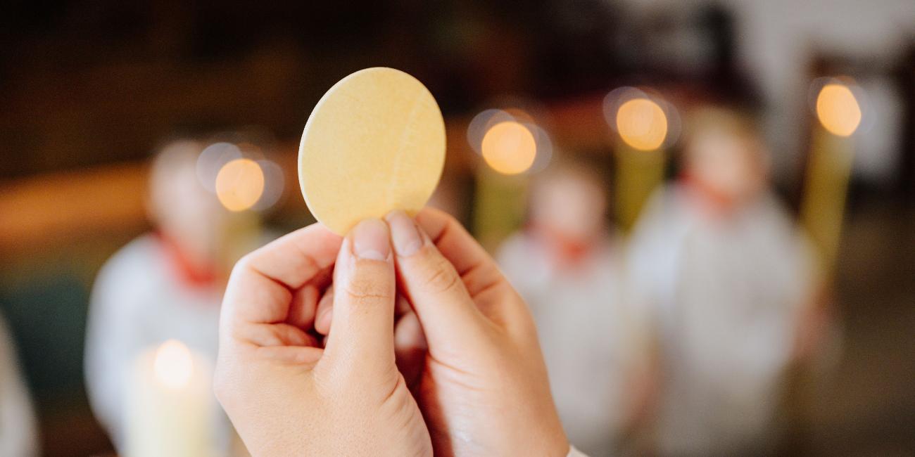 Zwei Hände halten die Hostie in die Höhe.