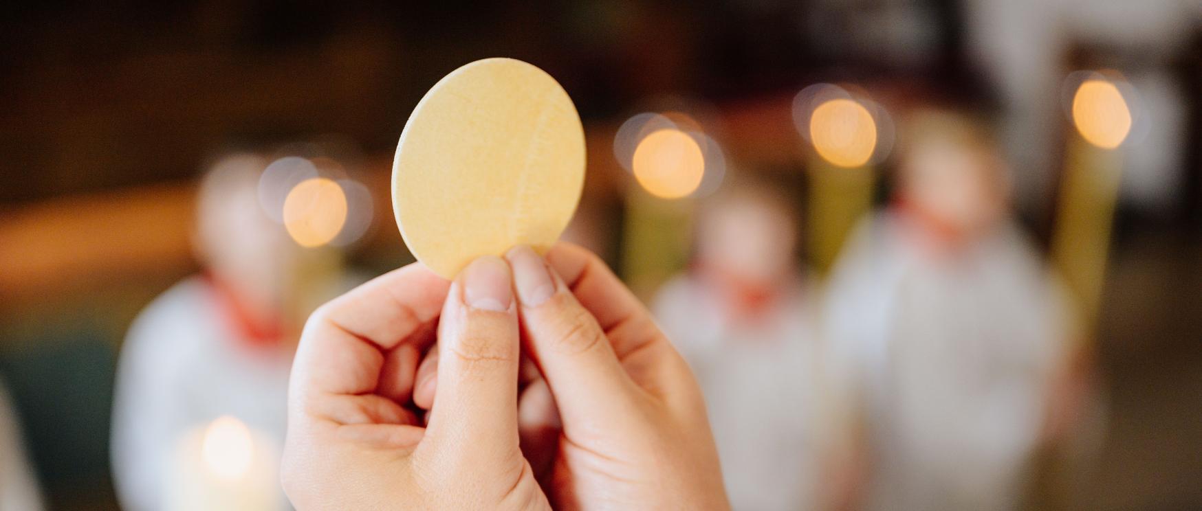 Zwei Hände halten die Hostie in die Höhe.