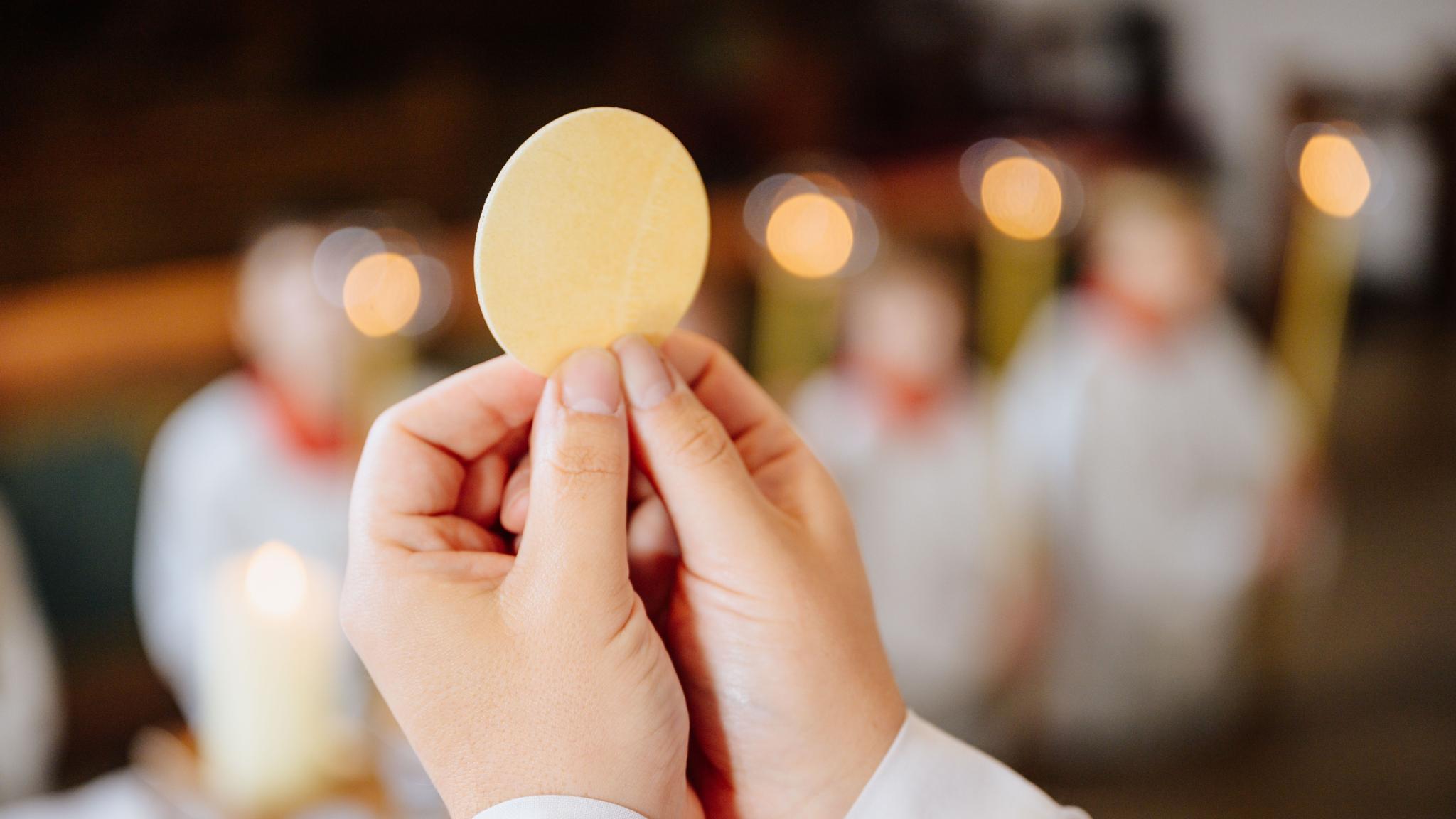 Zwei Hände halten die Hostie in die Höhe.