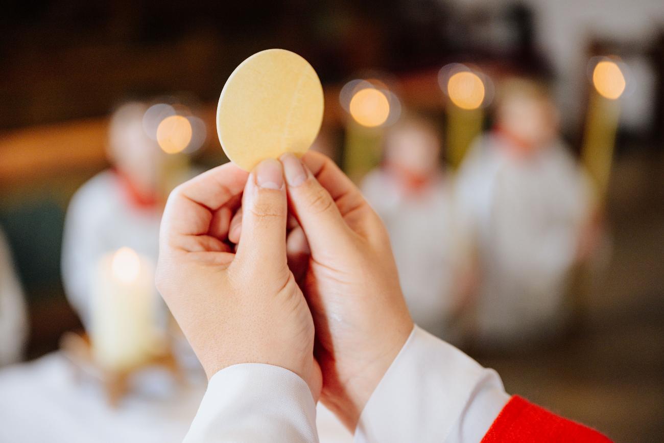 Zwei Hände halten die Hostie in die Höhe.