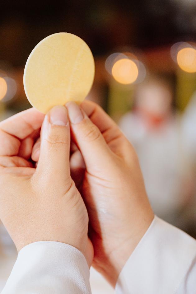 Zwei Hände halten die Hostie in die Höhe.