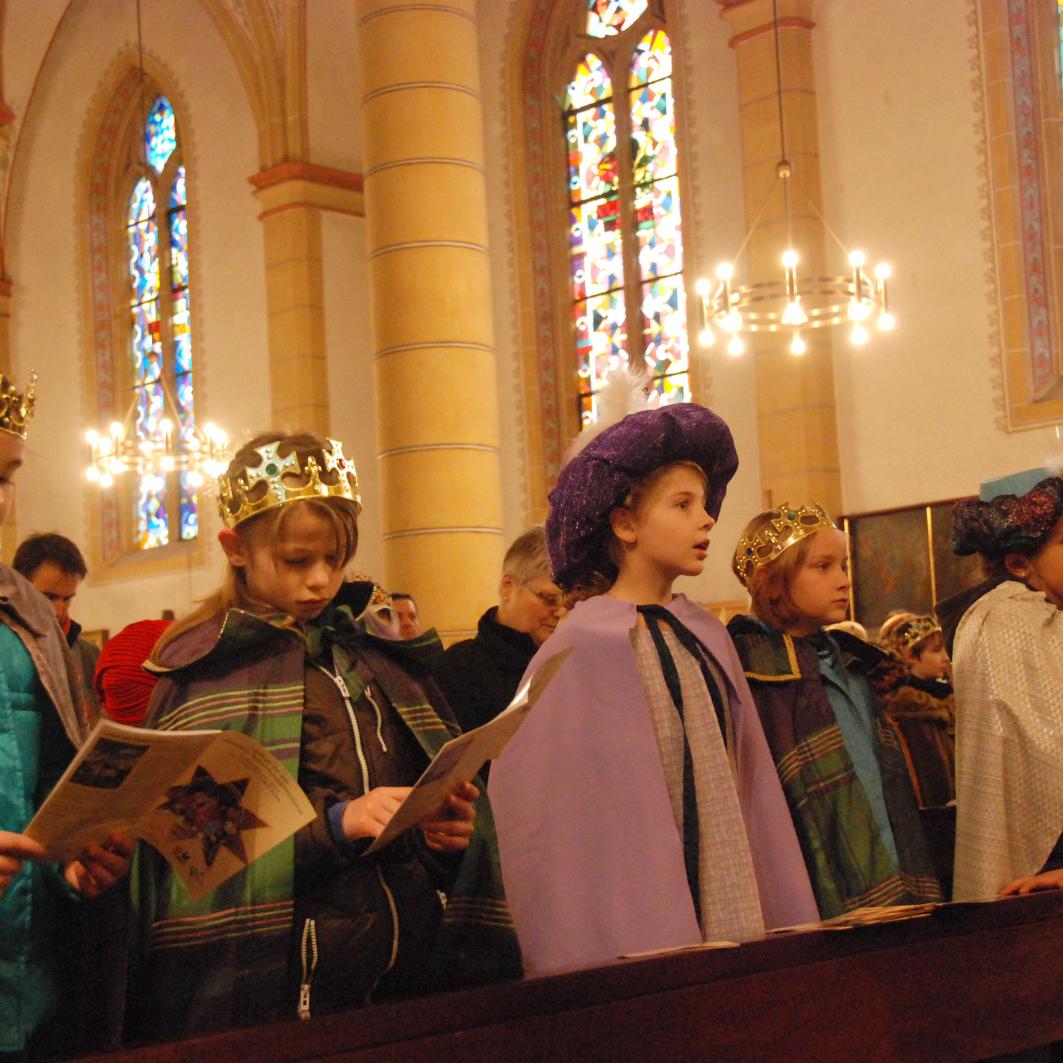 Sternsinger stehen in der Kirchenbank und singen.