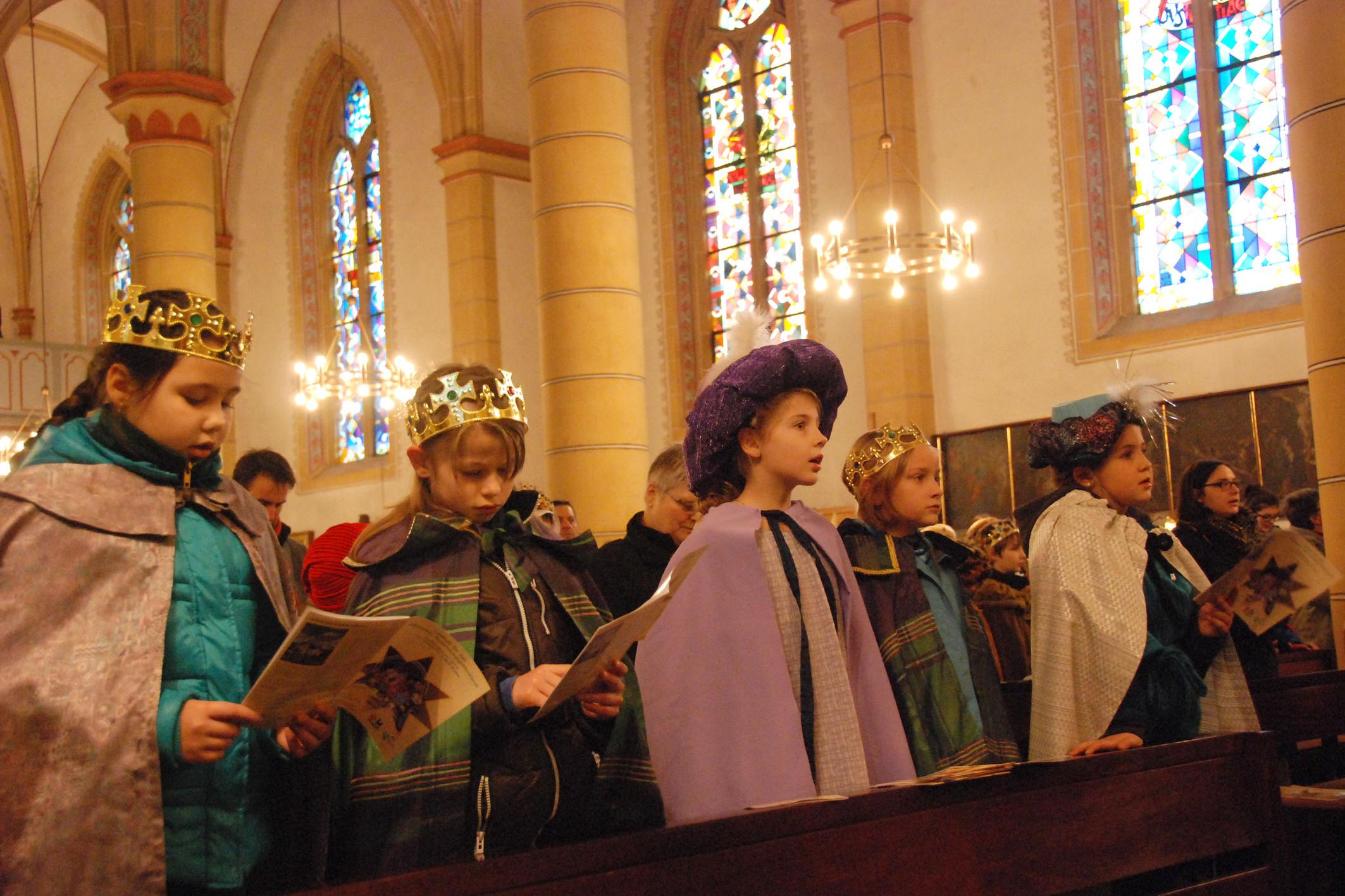 Sternsinger stehen in der Kirchenbank und singen.