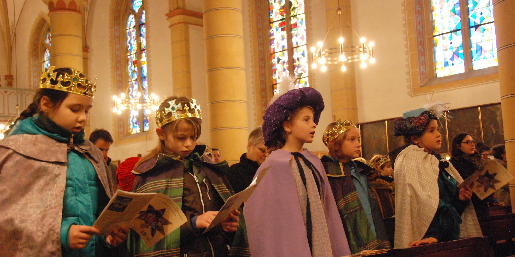 Sternsinger stehen in der Kirchenbank und singen.