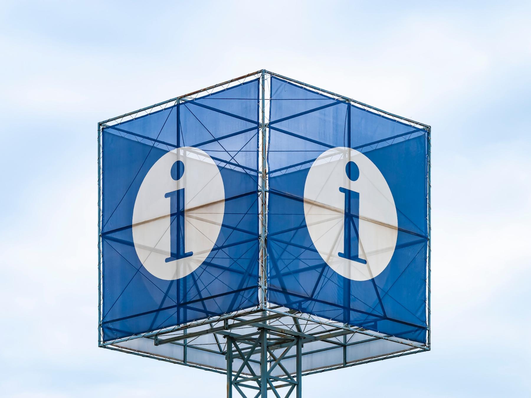 Man sieht einen blauen Kubus auf einem Mast. Auf jeder Seite ist ein weißer Kreis mit einem blauen i in der Mitte zu sehen