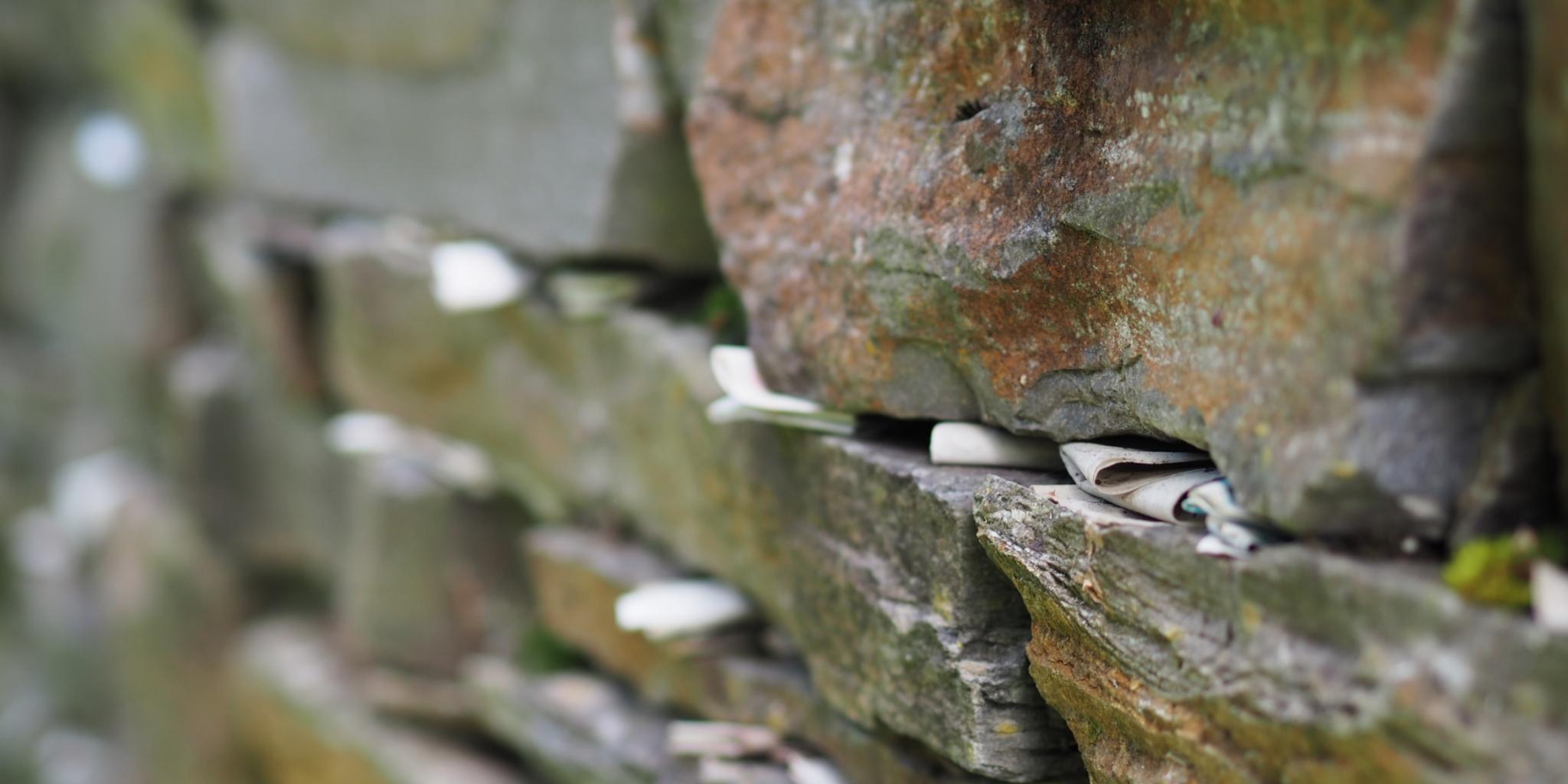Viele kleine Zettel zwischen den Steinen einer Mauer