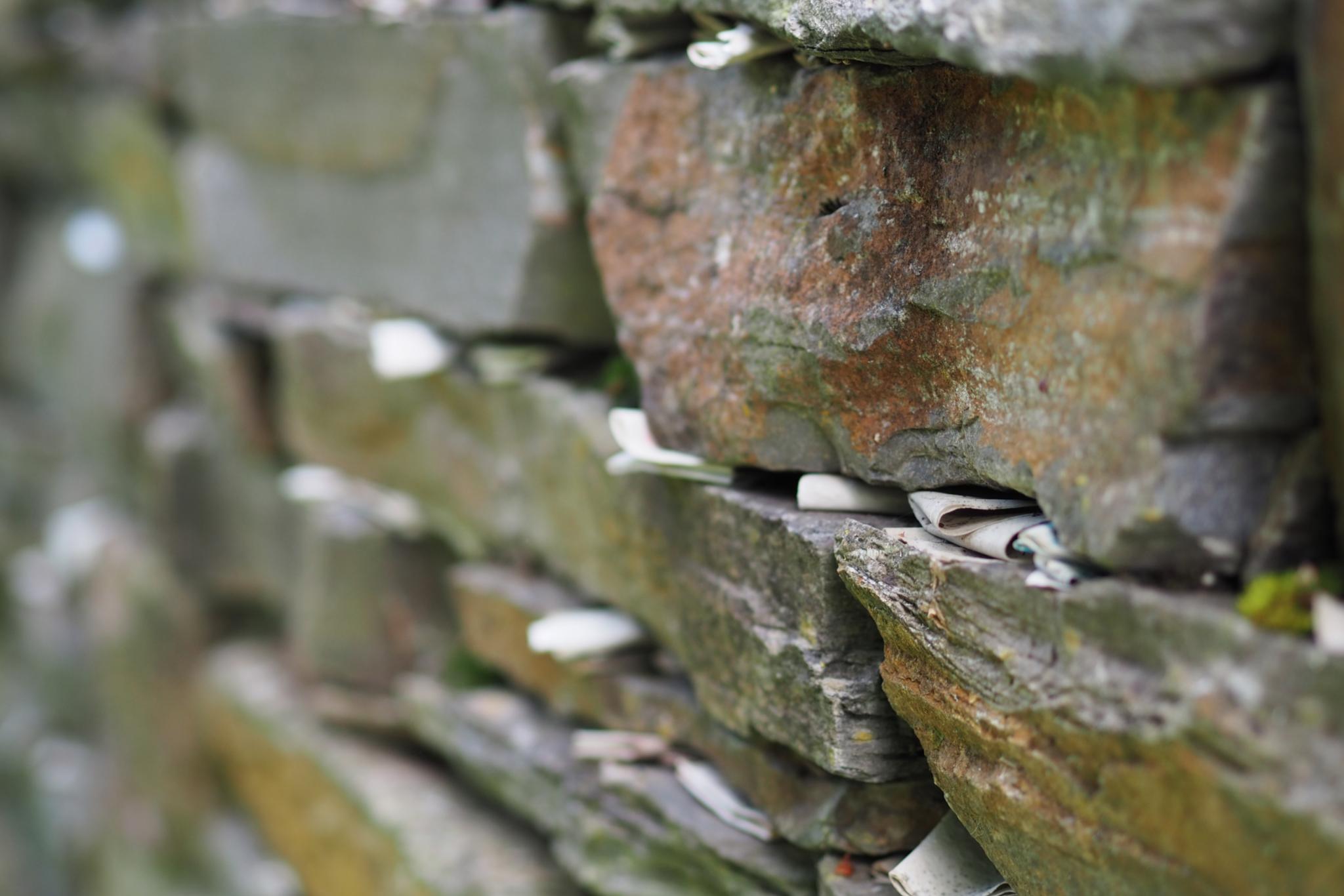 Viele kleine Zettel zwischen den Steinen einer Mauer
