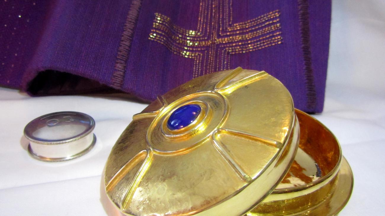 Auf einem Tisch steht eine halb geöffnete kleine Hostienschale. Daneben ein kleiner Behälter mit Salbe.