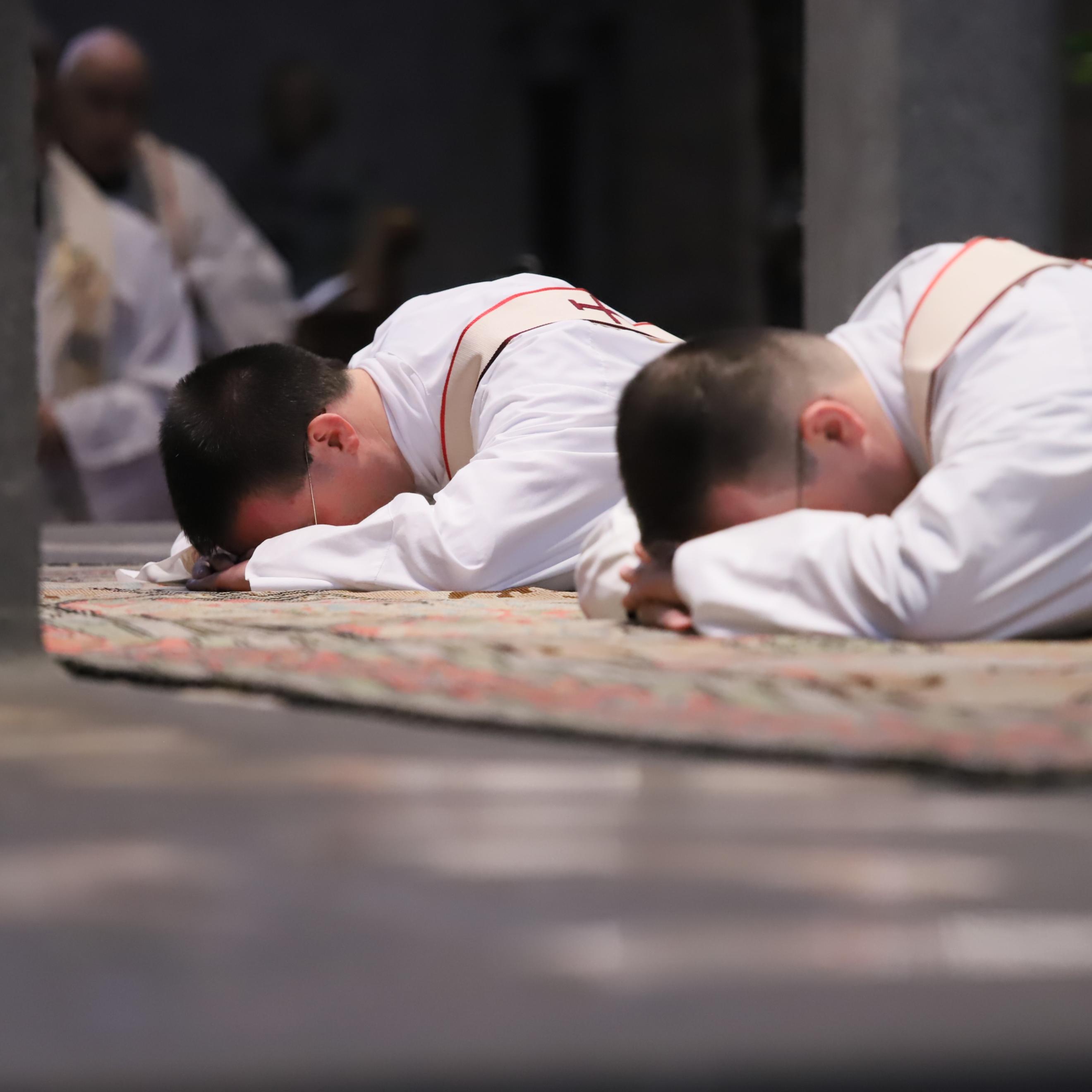 Zwei junge Männer liegen mit dem Gesicht nach unten vor dem Altar