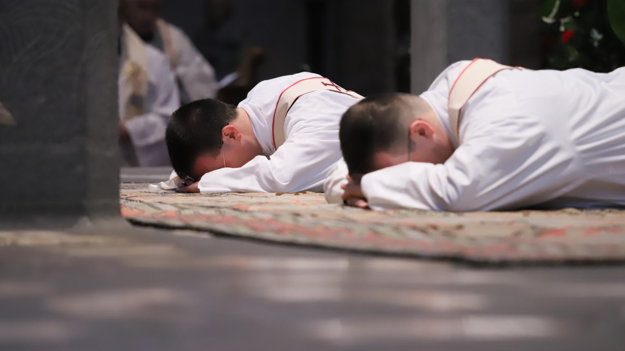 Zwei junge Männer liegen mit dem Gesicht nach unten vor dem Altar