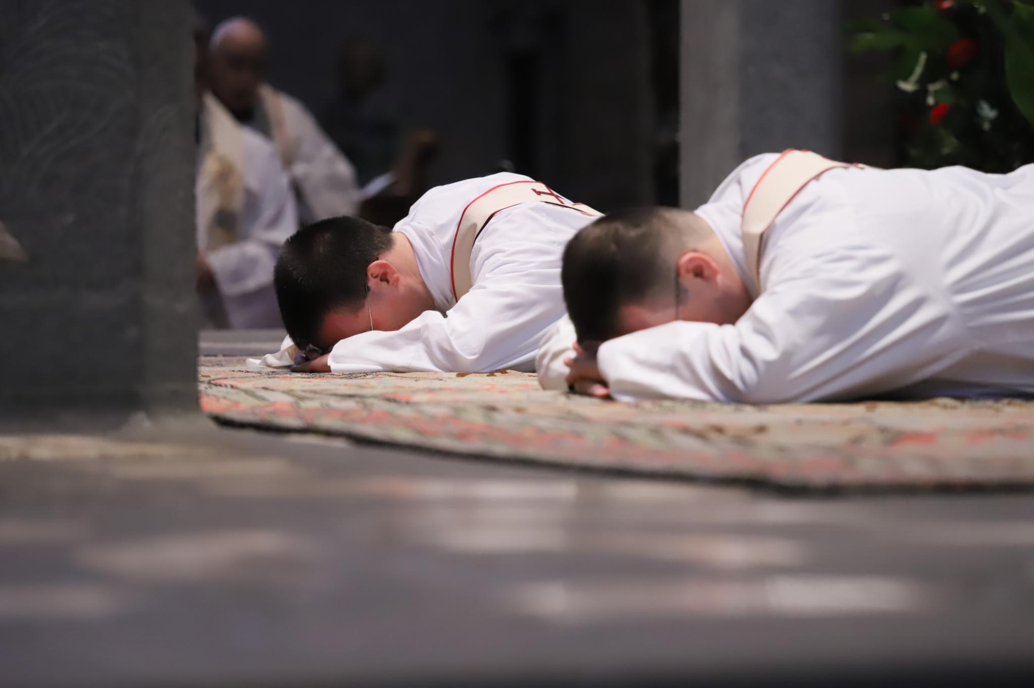 Zwei junge Männer liegen mit dem Gesicht nach unten vor dem Altar