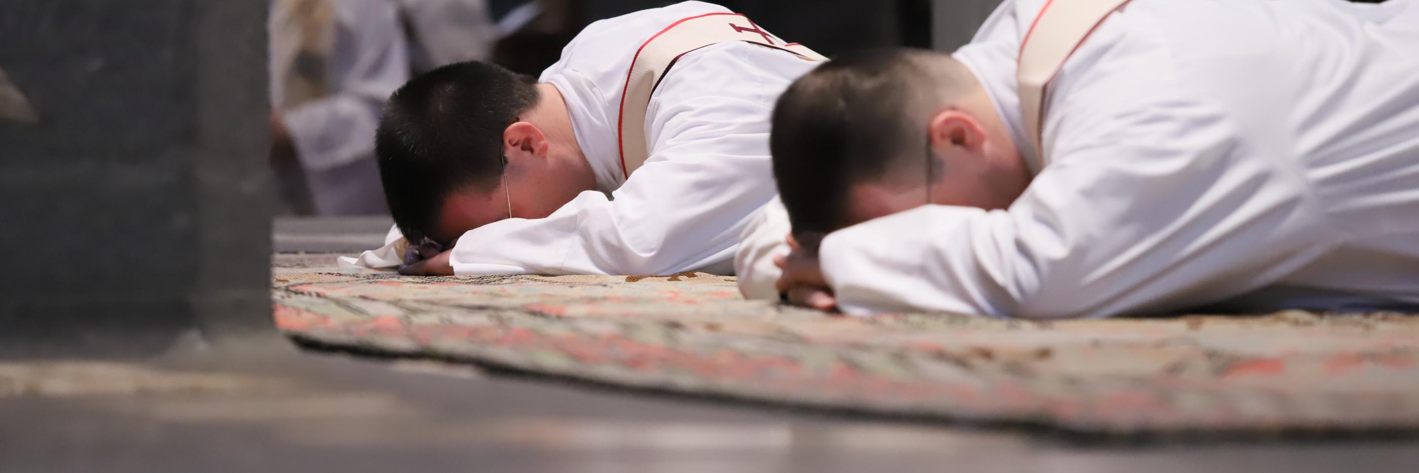 Zwei junge Männer liegen mit dem Gesicht nach unten vor dem Altar