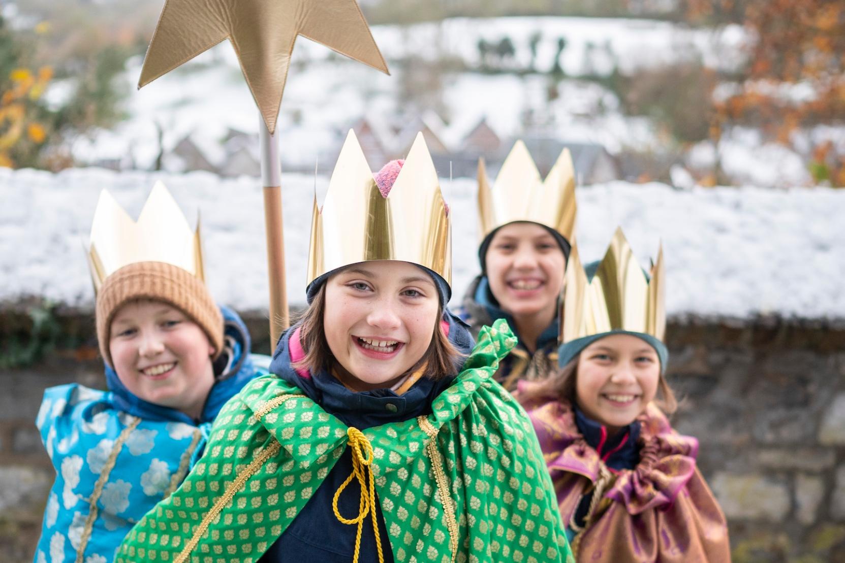 als Sternsinger verkleidete Kinder stehen als Gruppe zusammen, lächeln; einer hält einen Stern hoch, der vordere hält eine Spendendose