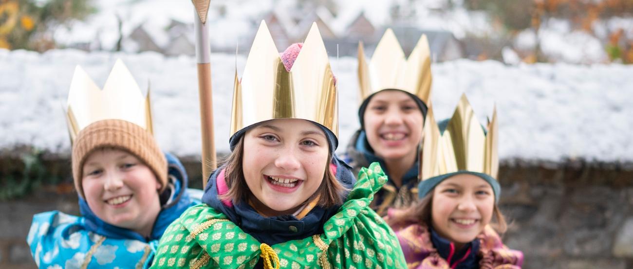als Sternsinger verkleidete Kinder stehen als Gruppe zusammen, lächeln; einer hält einen Stern hoch, der vordere hält eine Spendendose