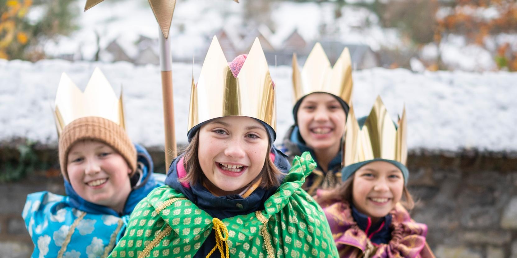 als Sternsinger verkleidete Kinder stehen als Gruppe zusammen, lächeln; einer hält einen Stern hoch, der vordere hält eine Spendendose