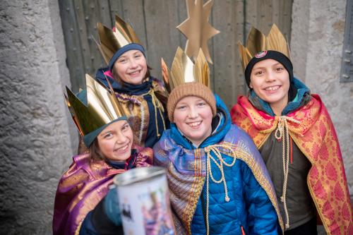 Vier als Sternsinger verkleidete Kinder mit Stern lächeln und halten eine Spendendose in die Kamera