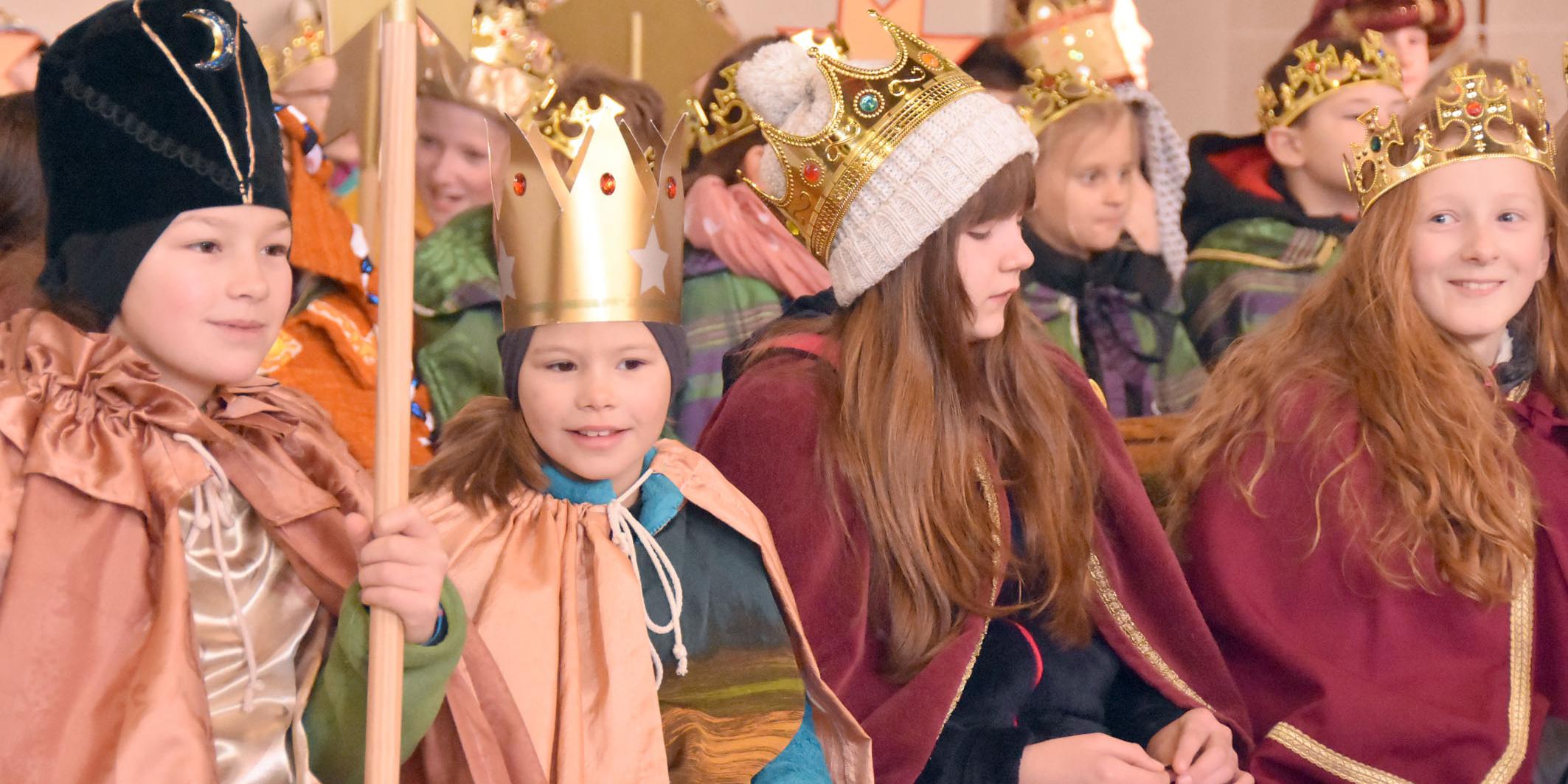 Kinder als Könige verkleidet sitzen in Gruppen zusammen in der Kirche