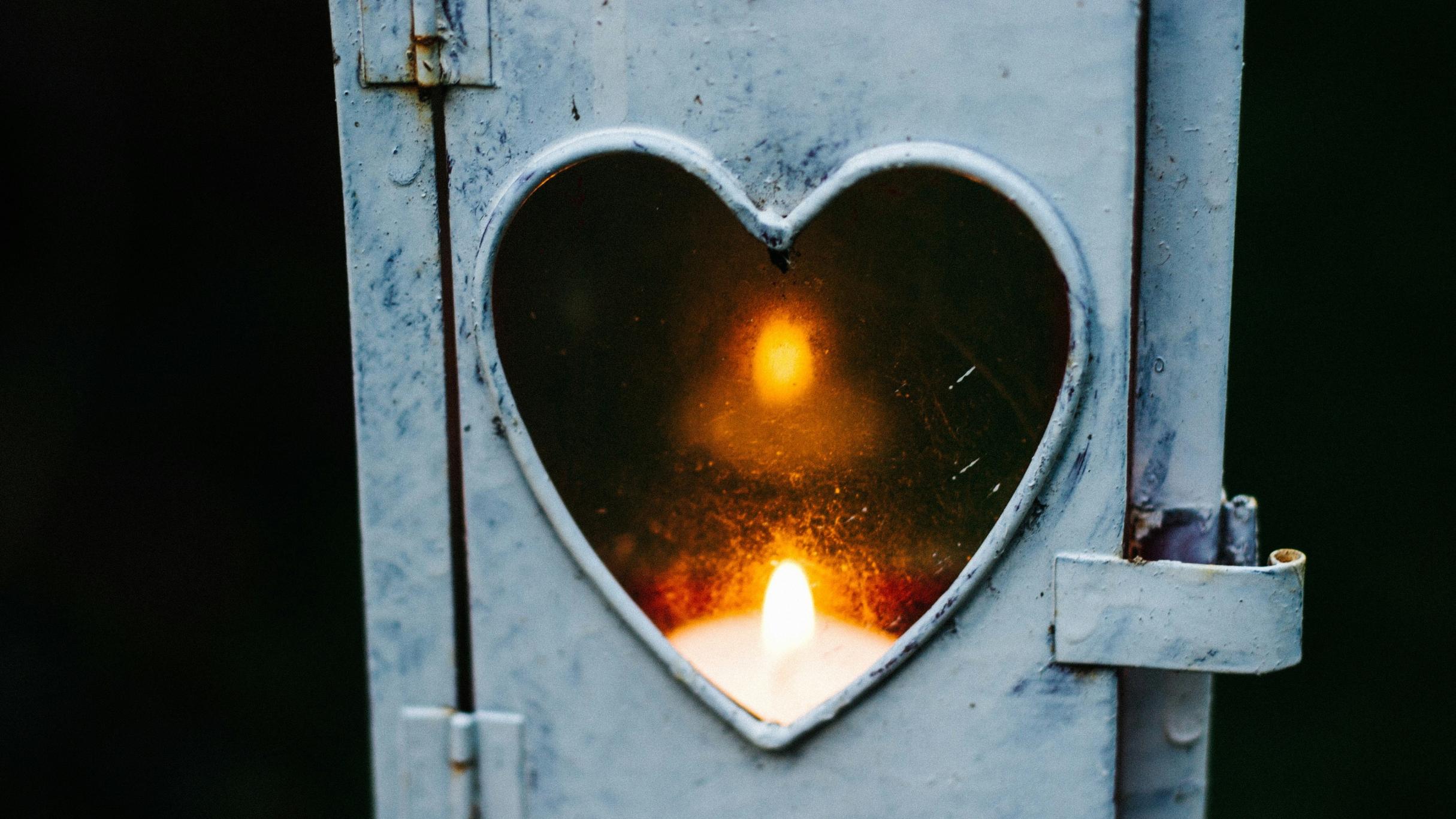 Ein Teelicht leuchtet in einer Laterne, deren Fenster ein kleines Herz ist